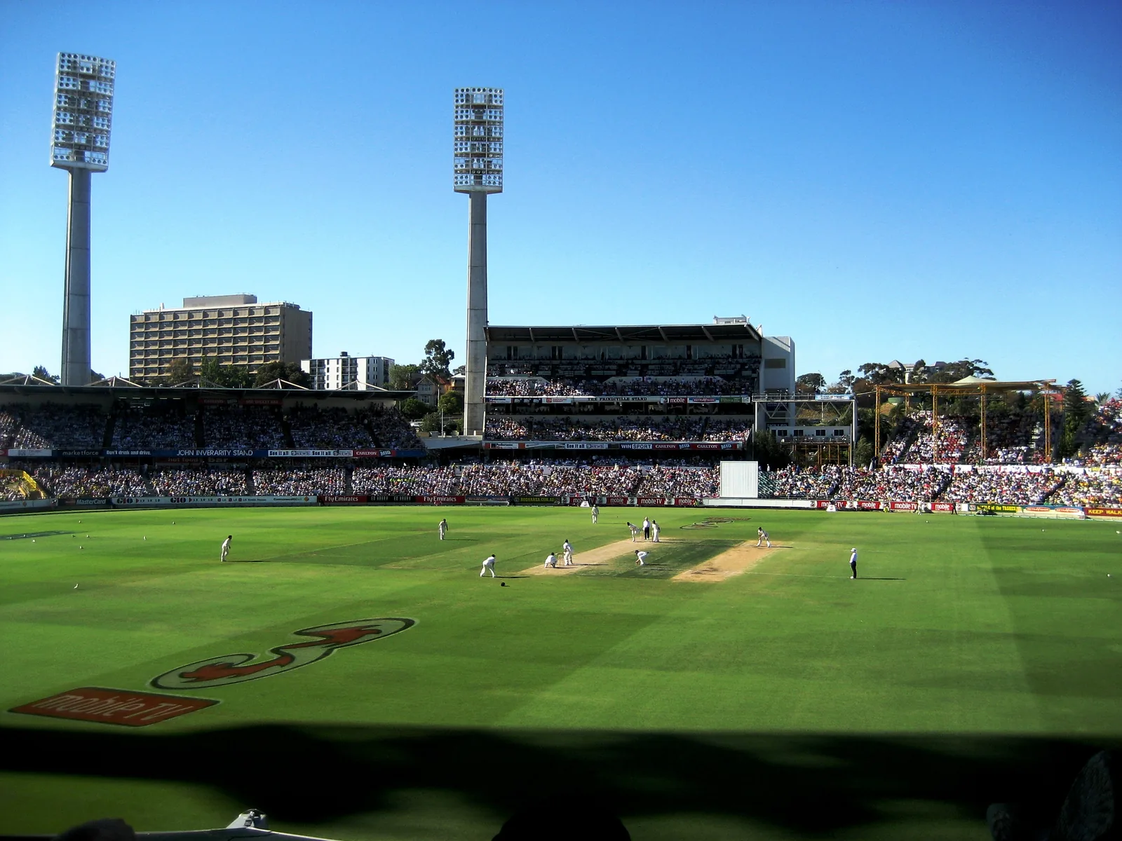 Cricket match underway at Perth's WACA Ground with the central pitch, stands and floodlight towers visible